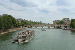 Boat tour on the Seine River in Paris, scenic cityscape with historic bridges and lush green trees.