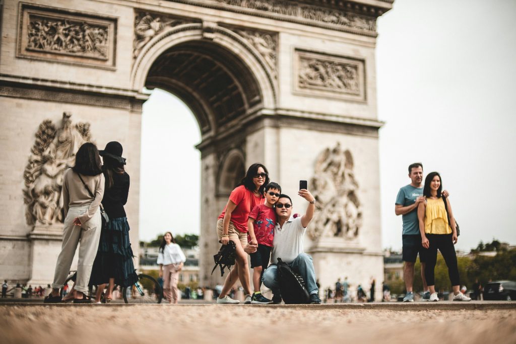 People taking selfies and exploring near the Arc de Triomphe in Paris, France. Travelers enjoying sightseeing at a famous tourist landmark.