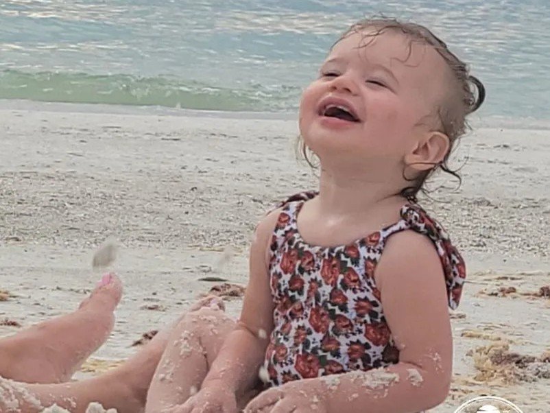 Joyful toddler girl playing on the beach with sand and ocean in the background, enjoying a beach vacation.